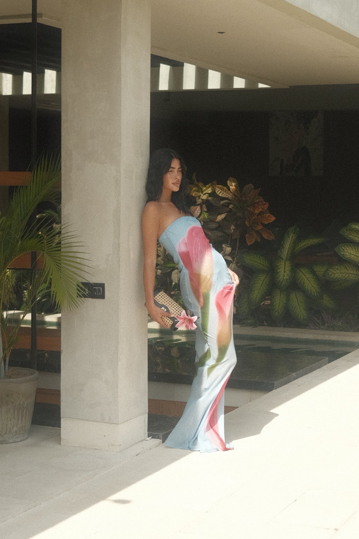 Person in blue and pink dress with a building and plants in the background