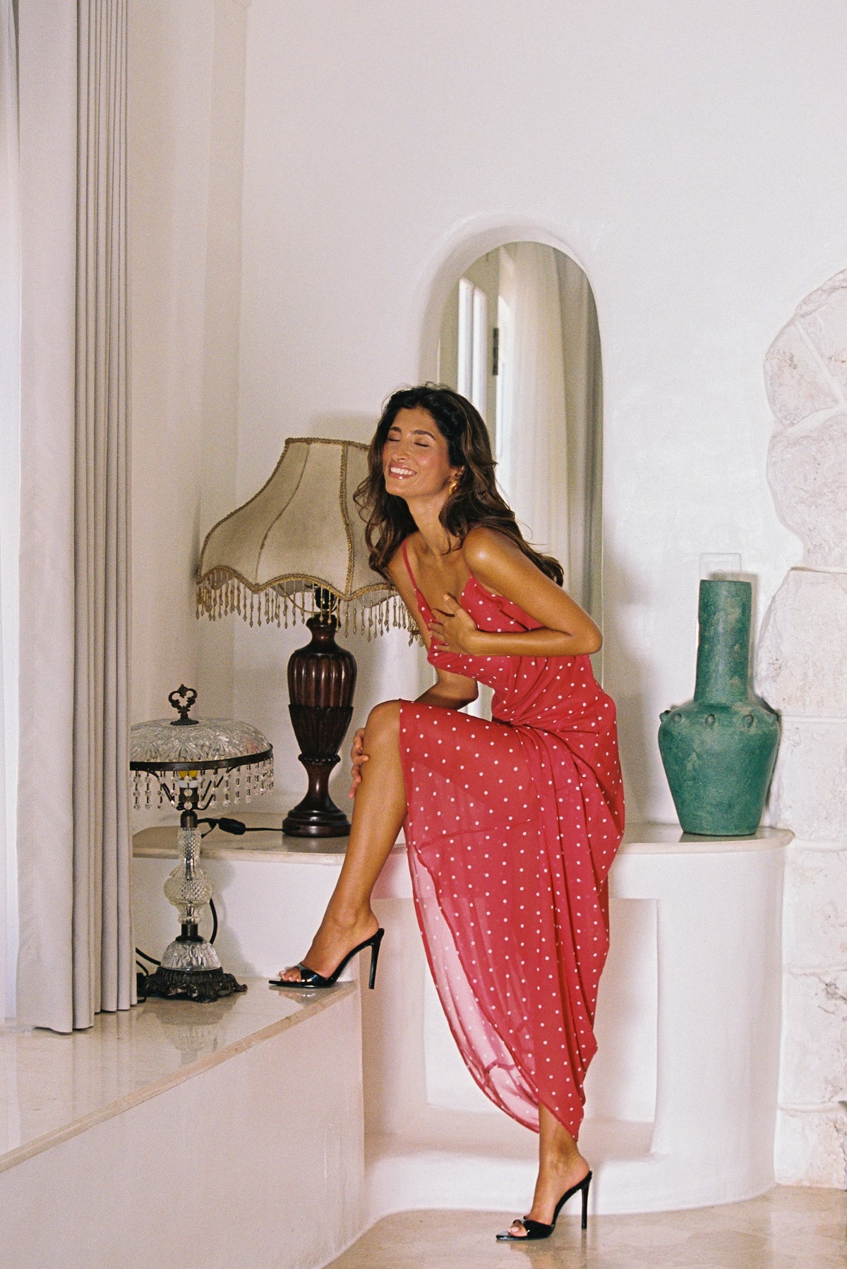 Woman in a red dress sitting on a white ledge with decorative items around her.